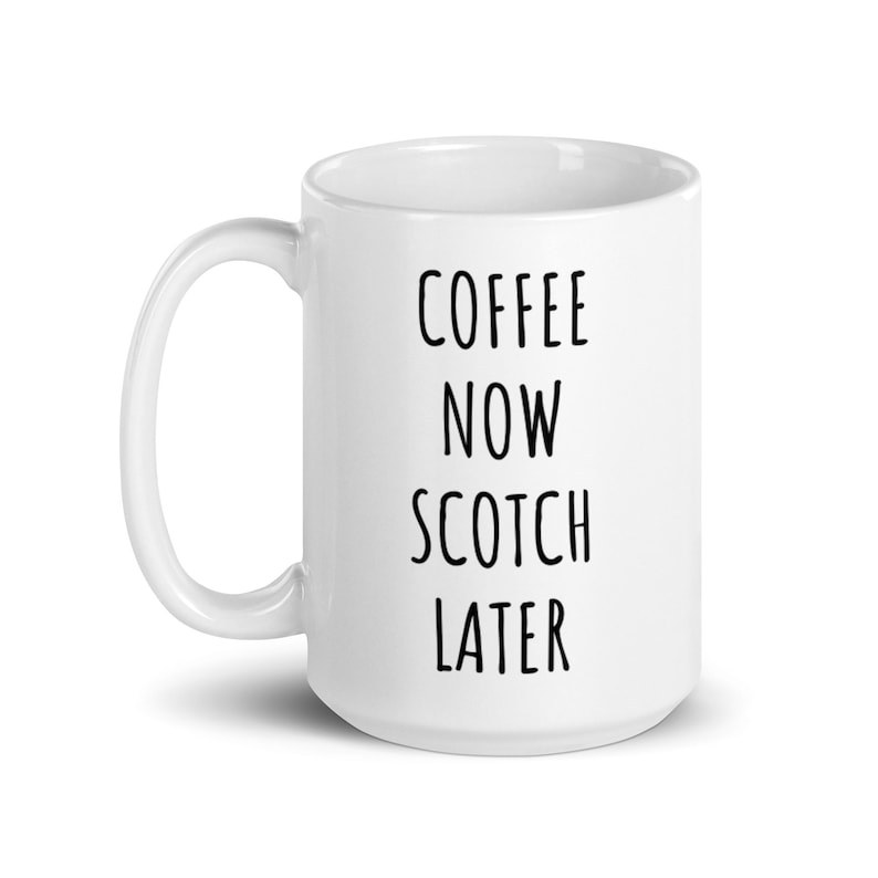 May include: White ceramic coffee mug with the words "COFFEE NOW SCOTCH LATER" printed in black, sans-serif font. The mug has a curved handle and a glossy finish, suitable for hot beverages.