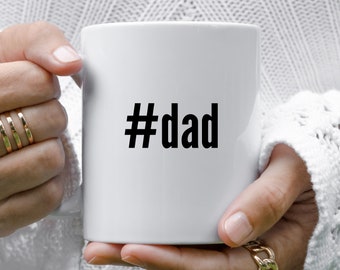 Op de afbeelding: Een witte keramische mok met een zwarte hashtag en het woord "dad" erop gedrukt.