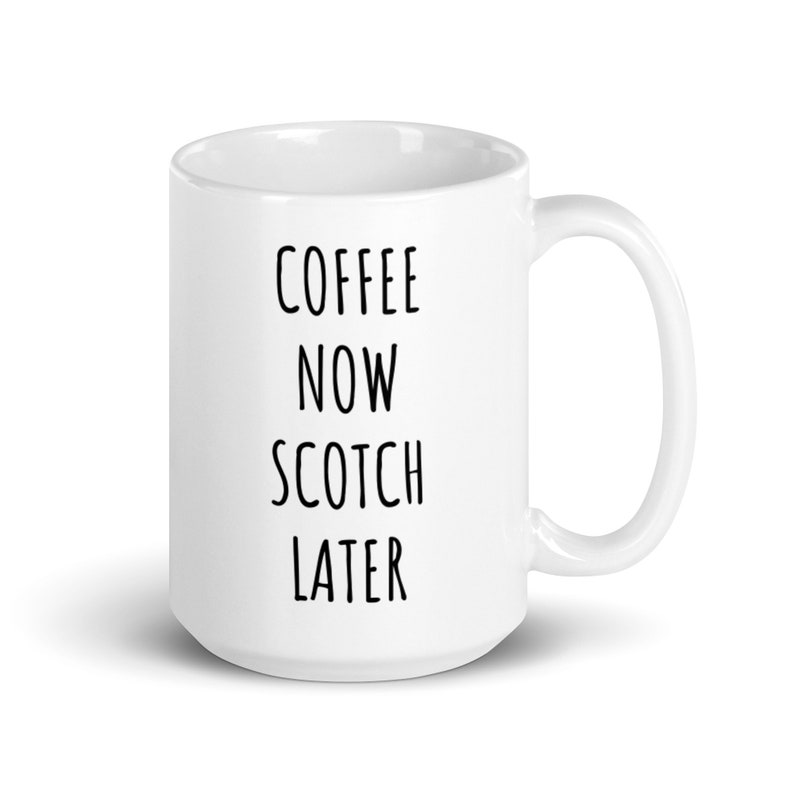 May include: White ceramic coffee mug with the text "COFFEE NOW SCOTCH LATER" in black, vertically aligned. The mug has a curved handle and a glossy finish, suitable for hot beverages. A simple, yet humorous design.