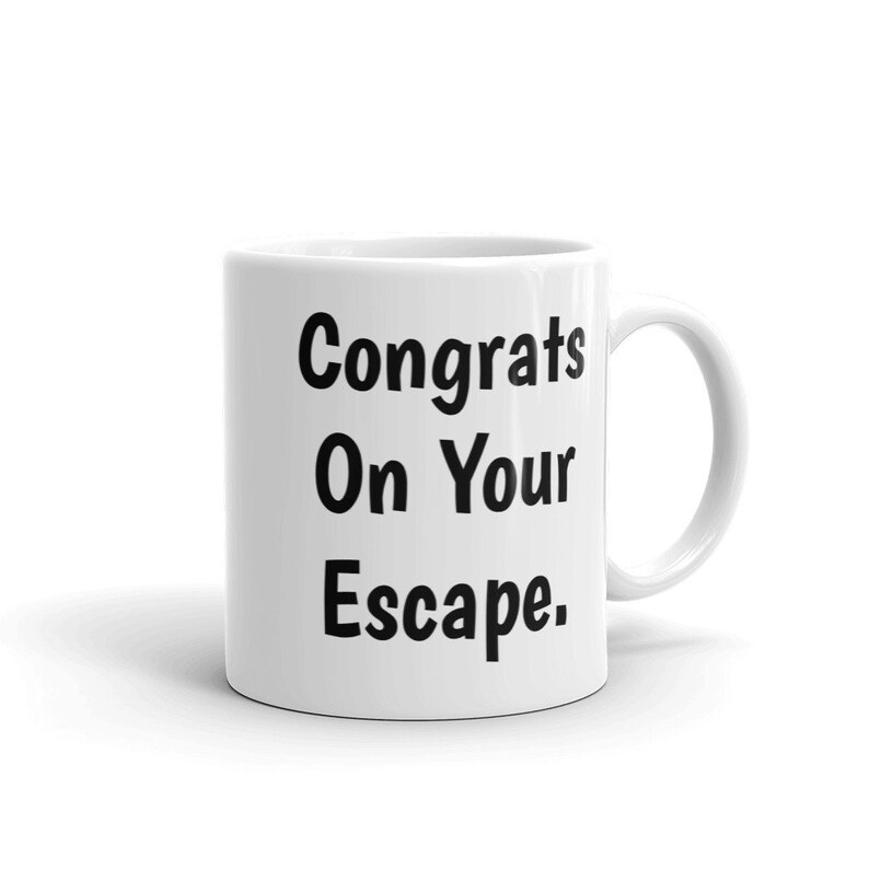 May include: White ceramic mug with black text that reads "Congrats On Your Escape."