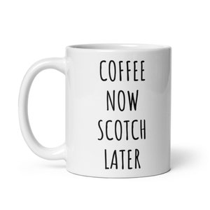 May include: White ceramic coffee mug with the text "COFFEE NOW SCOTCH LATER" in black, sans-serif font. The mug has a curved handle and a glossy finish. The mug is designed for hot beverages.