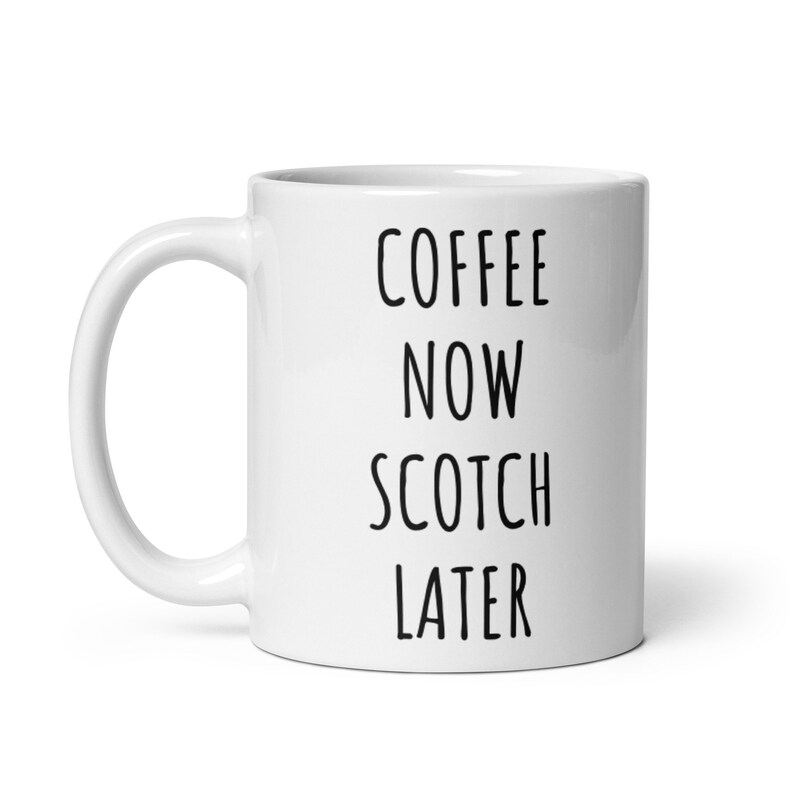May include: White ceramic coffee mug with the text "COFFEE NOW SCOTCH LATER" in black, sans-serif font. The mug has a curved handle and a glossy finish. The mug is designed for hot beverages.