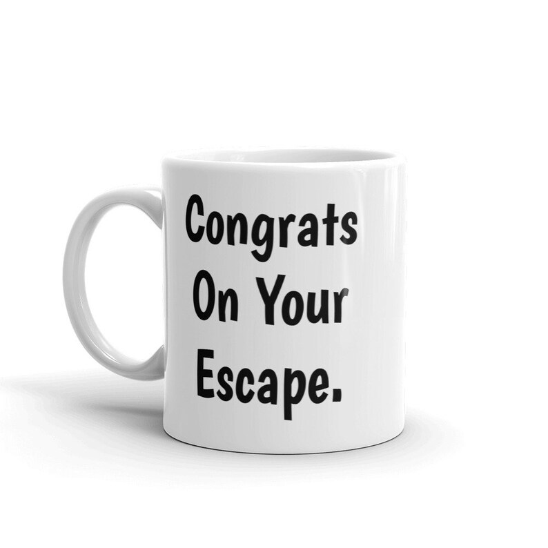 May include: White ceramic coffee mug with black text that reads "Congrats On Your Escape."