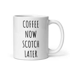 May include: White ceramic mug with a curved handle. The mug features the text "COFFEE NOW SCOTCH LATER" in black, bold, sans-serif font. The mug is designed for hot beverages.