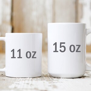 Op de afbeelding: Twee witte keramische mokken met zwarte tekst. De kleinere mok is 11 oz en de grotere mok is 15 oz.