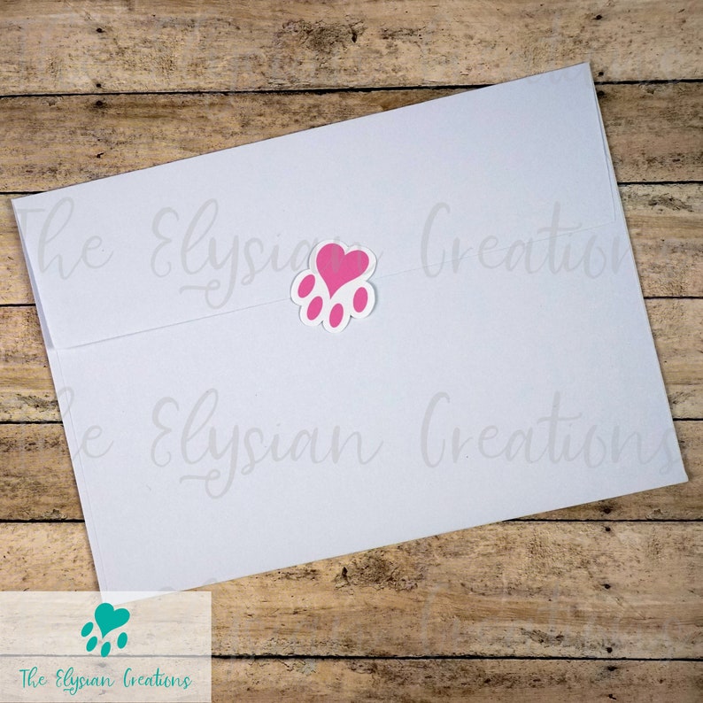 K&ouml;nnte beinhalten: Ein wei&szlig;er Umschlag mit einem rosa Pfotenabdruck-Aufkleber mit einem Herz in der Mitte. Der Text "The Elysian Creations" befindet sich am unteren Rand des Umschlags.