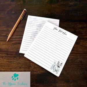 May include: Two white lined notepads with a West Highland White Terrier illustration and the text "Your Text Here". A gold pen rests on a dark wood surface. The Elysian Creations logo is visible.