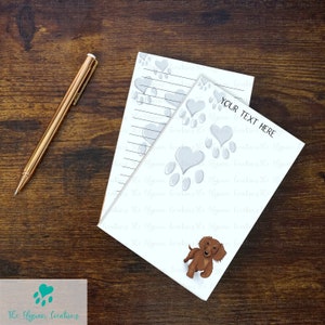 May include: Two white lined notepads with paw prints and hearts. The top notepad has the text "YOUR TEXT HERE". The bottom notepad has a cartoon image of a brown dachshund.