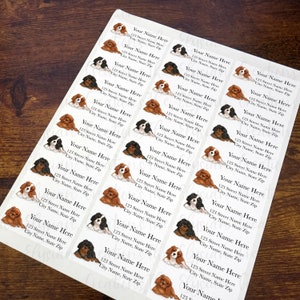 May include: A sheet of 24 personalised address labels featuring a cartoon illustration of two Cavalier King Charles Spaniel puppies. The labels are white with black text and a brown woodgrain background.