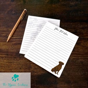 May include: Two white lined notepads with a brown dog illustration and the text "Your Text Here". A gold pen rests on the wooden surface. The Elysian Creations logo is visible at the bottom.