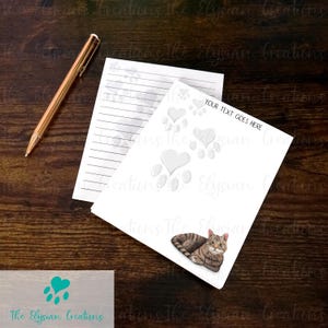 May include: White notepad with lined paper and a gray cat paw print design. The notepad has a white border and the text "YOUR TEXT GOES HERE" at the top. A tabby cat is lying down on the notepad.