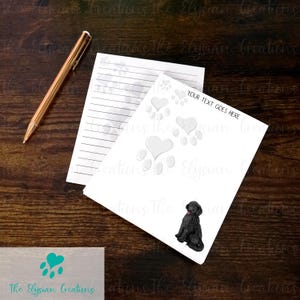 May include: White notepad with lined paper and a black and white illustration of a dog paw print with a heart on top. The notepad has a white background with gray paw prints and hearts. The text "YOUR TEXT GOES HERE" is printed on the notepad. A black dog is sitting on the notepad.