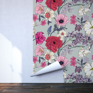 May include: A floral wallpaper with a green background and a variety of flowers in shades of pink, red, white, and purple. The wallpaper is being applied to a white wall.