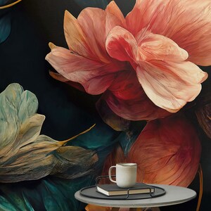 May include: A round gray side table with a wooden base and three legs. The table has a black tray on top with a white mug and a book. The table is in front of a dark background with a large pink flower and green leaves.