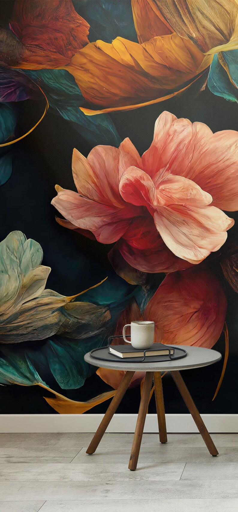 May include: A round gray side table with a wooden base and three legs. The table has a black tray on top with a white mug and a book. The table is in front of a dark background with a large pink flower and green leaves.