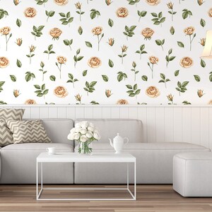 May include: A white couch with two pillows and a white coffee table in front of it. The wall behind the couch is covered in a wallpaper with a repeating pattern of light brown roses and green leaves.