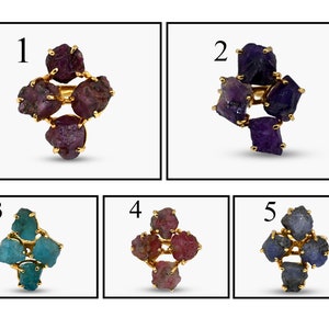 Pode incluir: Cinco anéis dourados, cada um com um grupo de pedras preciosas brutas. As pedras preciosas variam em cor, incluindo vermelho escuro, roxo, verde-azulado e azul. Os anéis são exibidos em um fundo branco.