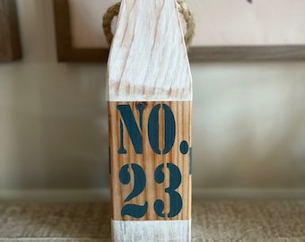 May include: White wooden block with a rope detail and the text "NO. 23" painted in dark blue.