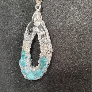 Peut inclure: Un collier en chaîne argent avec un pendentif en résine transparente orné d'un motif turquoise et paillettes argentées.