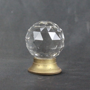 Könnte beinhalten: Ein klarer Glasknauf mit facettiertem Design, montiert auf einer Messingbasis.