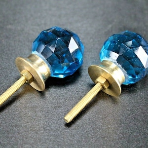 May include: Two blue glass cabinet knobs with brass bases and screws. The knobs are faceted and have a shiny finish.