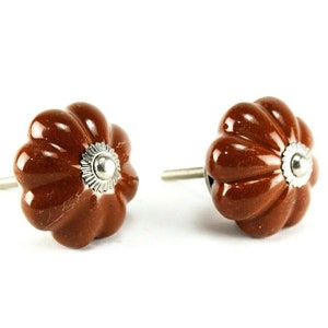 Pode incluir: Dois botões de armário de cerâmica marrom com um design canelado e um detalhe em metal prateado.