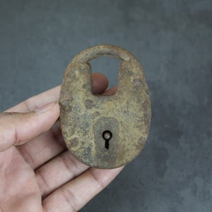 May include: A rusty metal padlock with a keyhole. The padlock is in the shape of a U with a rounded top and bottom. The padlock is held in a hand.