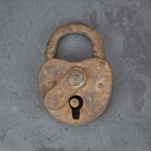 May include: A rusty heart-shaped padlock with a keyhole and a metal latch. The padlock is on a gray background.