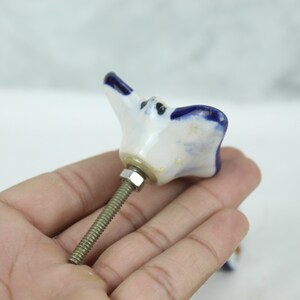 May include: White ceramic cabinet knob with a blue flower design and a silver screw.