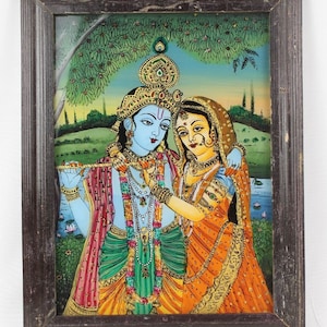 May include: A framed painting depicting a couple in a colorful, traditional Indian style. The man is wearing a blue and green outfit with a crown and jewelry, while the woman is wearing an orange and gold outfit with a head covering. The painting is set against a background of green trees and a blue sky.
