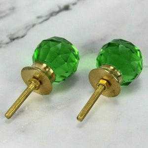 May include: Two green glass cabinet knobs with gold metal bases and screws. The knobs are faceted and have a shiny finish.