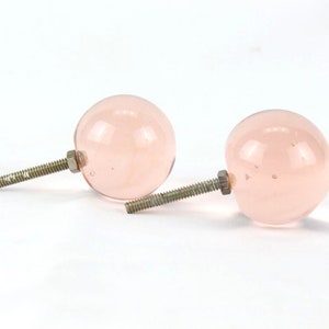 Może przedstawiać: Dwa różowe szklane gałki do szafek ze srebrnymi śrubami.