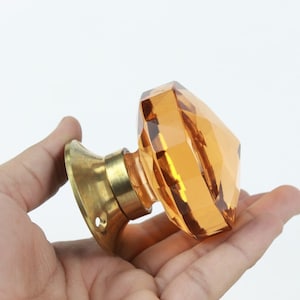 Könnte beinhalten: Ein facettierter Türknauf aus bernsteinfarbenem Glas mit Messingsockel.