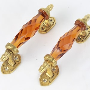 Op de afbeelding: Twee deurknopjes van amberkleurig glas met een facetgeslepen ontwerp en messing bases.