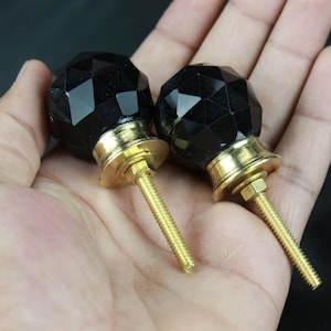 May include: Two black faceted glass cabinet knobs with gold metal bases and screws.