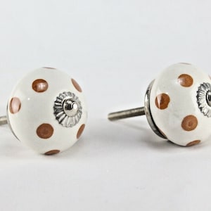 Peut inclure: Deux boutons de cabinet en céramique blanche avec des pois marrons et des accents argentés.