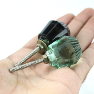 May include: Two cabinet knobs, one black and one green glass. The knobs have a threaded metal stem.