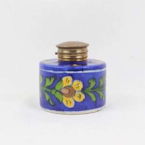 May include: A blue ceramic inkwell with a brass lid and floral designs in yellow, green, and pink.
