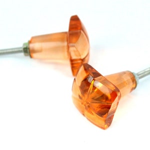 Op de afbeelding: Twee amberkleurige glazen kastknoppen met een stervormig ontwerp en zilveren schroeven.