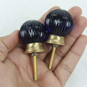 May include: Two blue glass cabinet knobs with a ribbed design and gold metal bases and screws.