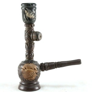 May include: A wooden smoking pipe with intricate carvings. The pipe has a round base, a long stem, and a small bowl at the top. The pipe is dark brown in color and has a natural wood finish.