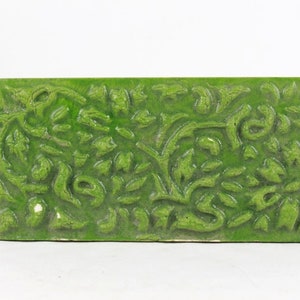 Puede incluir: Un azulejo de cerámica verde con un diseño floral en relieve. El azulejo tiene una superficie texturizada y está hecho de cerámica vidriada.
