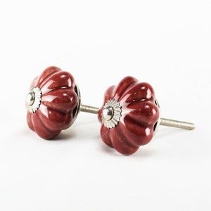 Könnte beinhalten: Zwei rote Keramik-Schrankknöpfe mit geriffeltem Design und silbernen Akzenten. Die Knöpfe haben eine Schraube auf der Rückseite zum Befestigen an einer Schranktür.