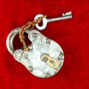 May include: A silver padlock with a key attached to it by a string. The padlock is labeled "50mm" and "K.F. ADAPT 33".
