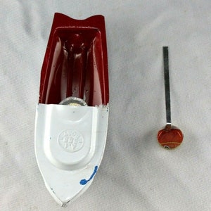 May include: A red and white toy boat with a metal oar. The boat has a white bottom with a blue stripe and a red top. The oar is made of metal and has a red and white handle.
