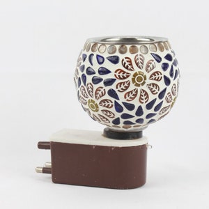 Puede incluir: Un calentador de aceite enchufable decorativo con una pantalla de vidrio de mosaico. La pantalla presenta un patrón floral con piezas de vidrio blancas, azules, marrones y doradas. La base es marrón con una parte superior blanca.