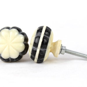 May include: Two decorative cabinet knobs with a black and white striped design. One knob has a flower-shaped design. The knobs are made of a smooth, white material.