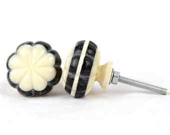 May include: Two decorative cabinet knobs with a black and white striped design. One knob has a flower-shaped design. The knobs are made of a smooth, white material.