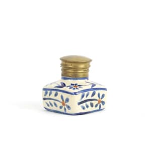 Puede incluir: Un tintero de cerámica blanca con un diseño floral azul y naranja y una tapa de latón.