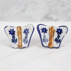 May include: A pair of ceramic butterfly-shaped drawer pulls with blue, green and brown floral designs.